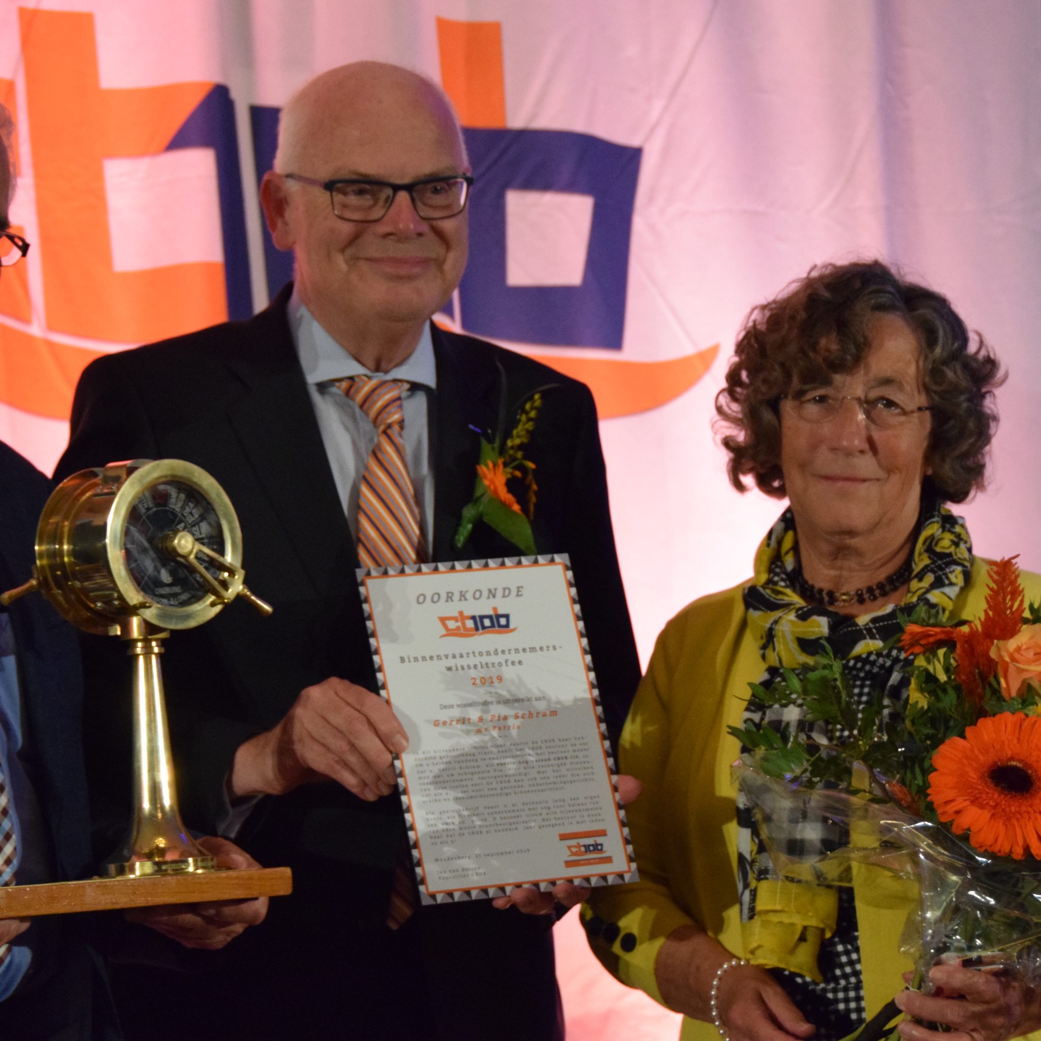 Al bijna 58 jaar is Gerrit Schram (links) lid van het CBOB. Als oudste nog varende lid kreeg hij de Binnenvaartondernemers Wisseltrofee uit handen van voorzitter Jan van Belzen (midden, met oorkonde). Schippersvrouw Pia Schram deelt volledig in de eer voor het varend familiebedrijf. (Foto Dirk van der Meulen)