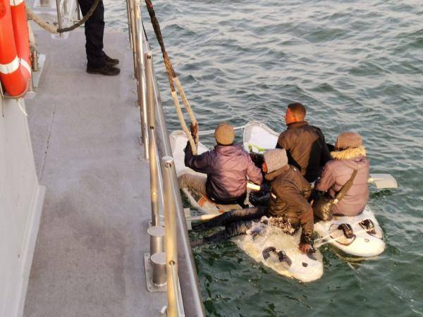 De vier migranten op hun vlotje van surfplanken. Ze dragen wel dikke jassen maar hebben geen zwemvesten of andere reddingsmiddelen aan boord. (foto: Gendarmerie Maritime)