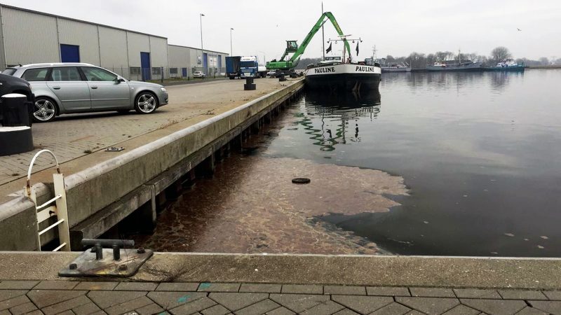 De vervuiling zoals die de volgende dag werd aangetroffen in de haven van Farmsum. Het schip op de foto heeft niets met de illegale lozing te maken (foto: Mark Heikens).