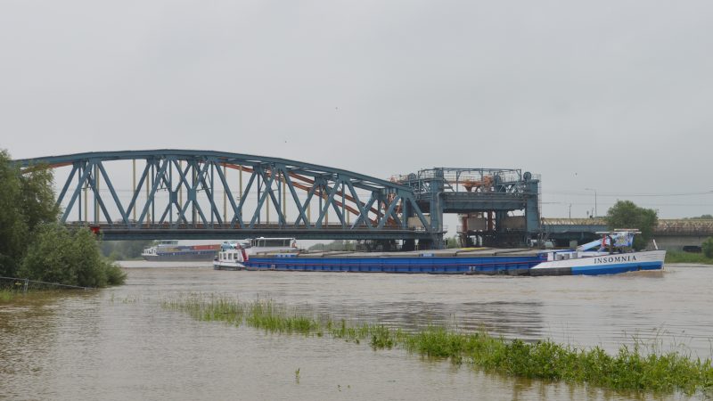 Een afvarig containerschip wordt gaande gehouden met de stroom op de kont in afwachting van een brugopening, terwijl de Insomnia net wel onder de vaste overspanning van de Zutphense bruggen past. (Foto Sander Wels)