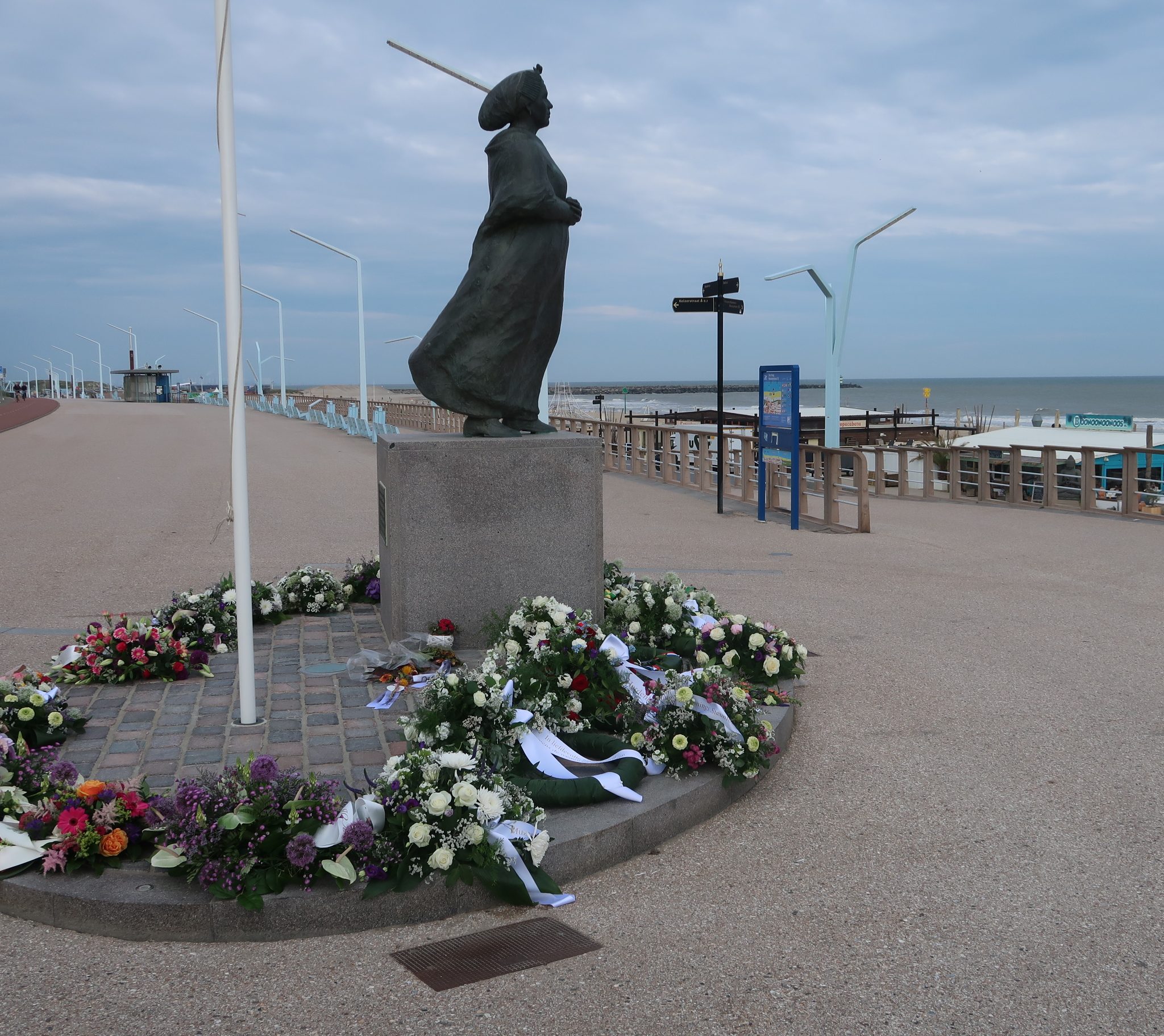 Bloemenkransen rondom het monument van de Scheveningse vissersvrouw die uitkijkt over zee. (Foto W.M. den Heijer)