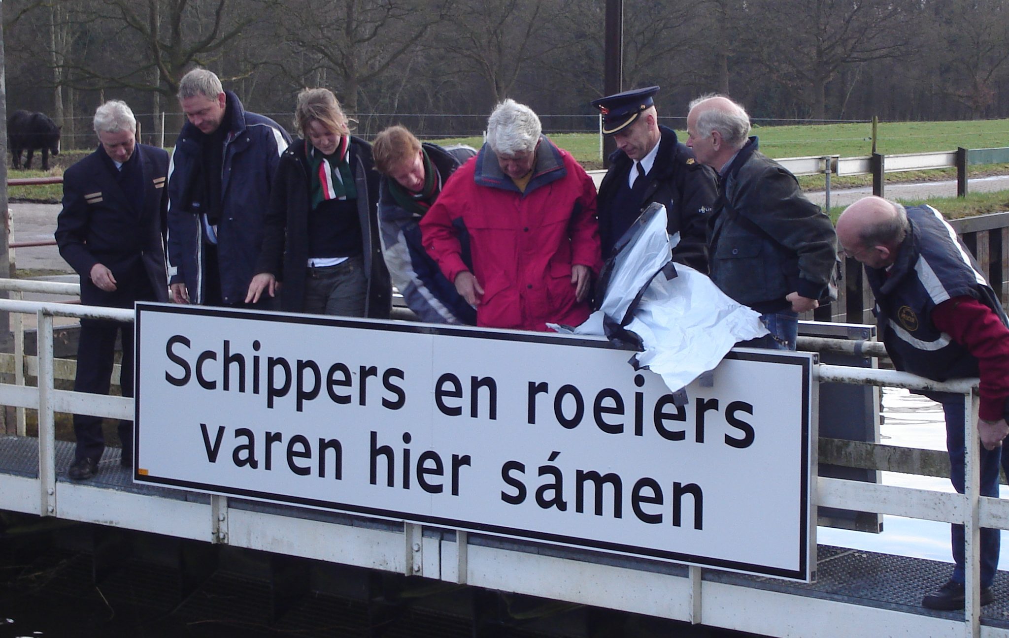 Medewerkers van de politie, Rijkswaterstaat, belangenbehartigers van Koninklijke Schuttevaer en voorzitters van roeiverenigingen onthullen in 2007 een billboard op de sluisdeur in Delden.