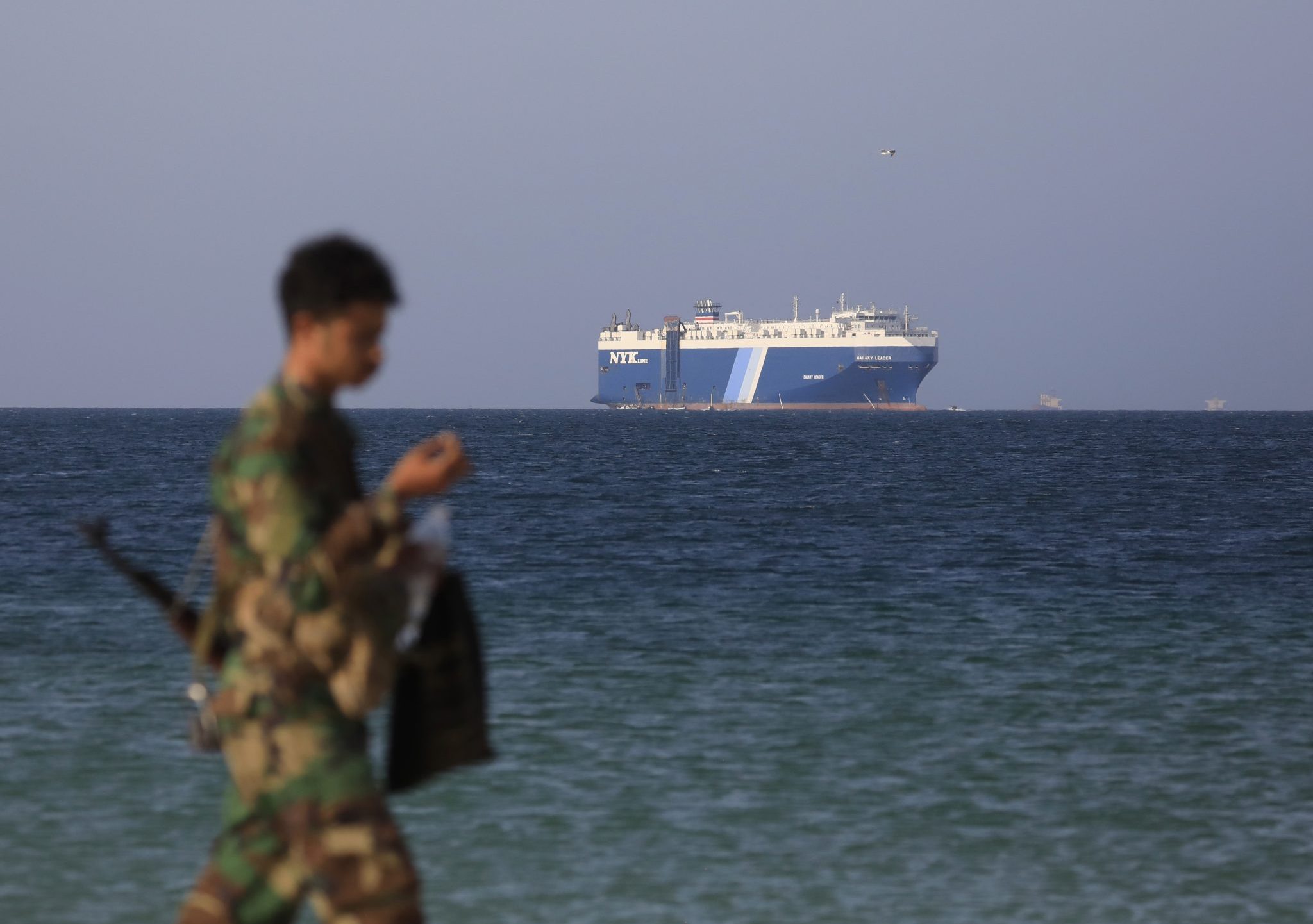 Een Houthi-soldaat in Jemen met op de achtergrond het ingenomen schip Galaxy Leader.